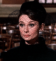 a woman wearing a veil and a hat looks at the camera