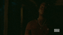 a man is standing in the dark wearing a necklace and a red shirt .