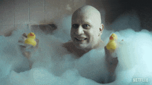 a bald man is in a bathtub holding two yellow rubber ducks with a netflix logo in the corner