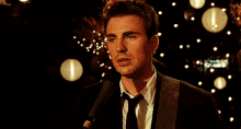 a man in a suit singing into a microphone with a guitar in the background