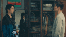 two men are standing in front of a closet with clothes on it