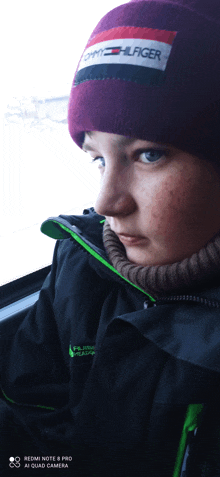 a boy wearing a tommy hilfiger beanie looks out the window