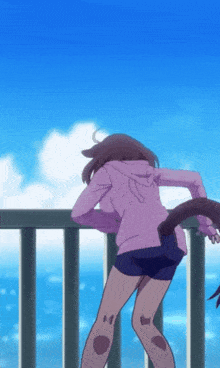 a girl in a purple hoodie and shorts is standing on a balcony overlooking the ocean