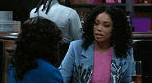 two women are sitting at a bar talking to each other . one of the women is wearing a blue jacket .