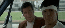 a man with a bandage on his head is sitting next to another man in a car