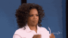 a woman with curly hair is wearing a white shirt and holding a piece of paper in her hand .