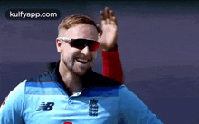a man wearing sunglasses and a new balance shirt waves his hand .