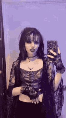 a woman is taking a selfie in front of a mirror while wearing a gothic outfit .