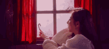 a woman is sitting in front of a window holding a candy cane and looking out .