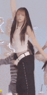 a woman in a white tank top and black pants stands with her arms in the air