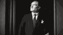 a black and white photo of a man in a suit and bow tie looking up .