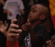 a person is holding a cell phone in front of a child wearing a give shirt