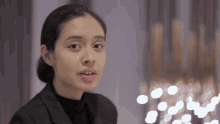 a woman wearing a black jacket and black turtleneck looks at the camera