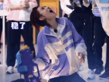 a man in a purple jacket is sitting on the floor with his mouth open and a group of people behind him .
