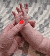 a baby 's hand is being held by a woman with red nails