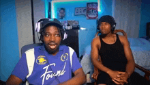 a man wearing headphones and a purple shirt is sitting next to another man in a chair .