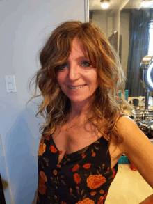 a woman in a black floral top smiles in front of a mirror