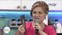 a woman in a pink shirt is holding a microphone in front of a sign that says kapamilya online live