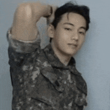a man in a military uniform is standing with his hand behind his head and looking at the camera .