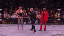 a wrestler in a red suit shakes hands with a man in a black suit