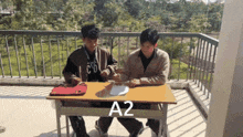 two boys sit at a table with a2 written on the table