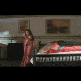 a woman in a red sari is standing in a bedroom next to a bed