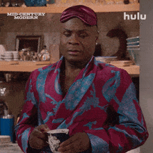 a man in a bathrobe is holding a cup of coffee in front of a sign that says hulu
