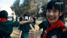 a girl giving a thumbs up in front of a sign that says " fever "