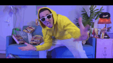 a man wearing sunglasses and a yellow hoodie is standing in front of a blue couch with lion wild chips on it