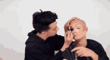a man applying makeup to another man 's face with a fan