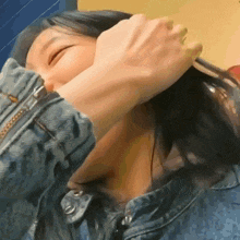 a woman wearing a denim jacket is covering her face with her hand