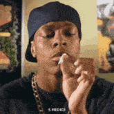 a man wearing a hat is smoking a cigarette and says s medici in the corner