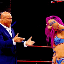 a wrestler with pink hair is talking to a man in a suit .