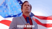 a man in a suit and tie is standing in front of an american flag with his hand on his chest