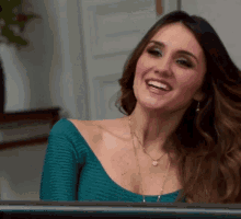 a woman wearing a green off the shoulder top and a necklace smiles