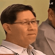 a man wearing glasses and a white shirt is sitting in front of a microphone with the letters lje on the bottom