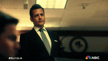 a man in a suit and tie is standing in front of a nbc logo