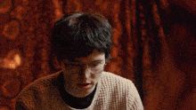 a young man wearing glasses and a tan sweater