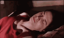 a woman is laying on a bed with her eyes closed . she is wearing a red tank top .