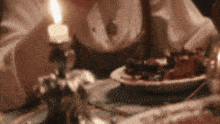 a person is sitting at a table with a candle lit and a plate of food .