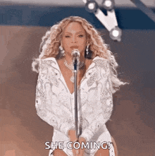 a woman in a white dress is singing into a microphone and says she is coming .