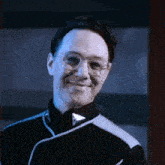 a man with glasses and a black jacket smiles for the camera