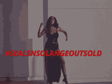 a woman in a black dress is dancing in front of a wall with #sealsnsolangeoutsold written in red letters