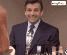 a man in a suit and tie is smiling in front of bottles of alcohol
