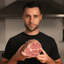a man in a black shirt holds a large piece of meat