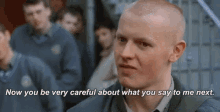 a man with a shaved head is talking to another man in a crowd .