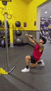 a man in a red tank top is pulling a cable in a gym