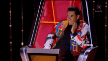a man in a colorful jacket sits in a chair on a television screen