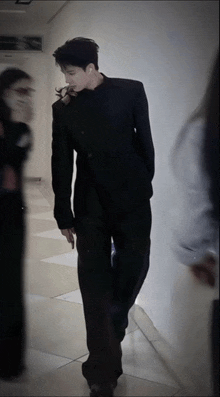 a man in a black suit stands in a hallway