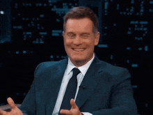 a man in a suit and tie is smiling with his hands in the air